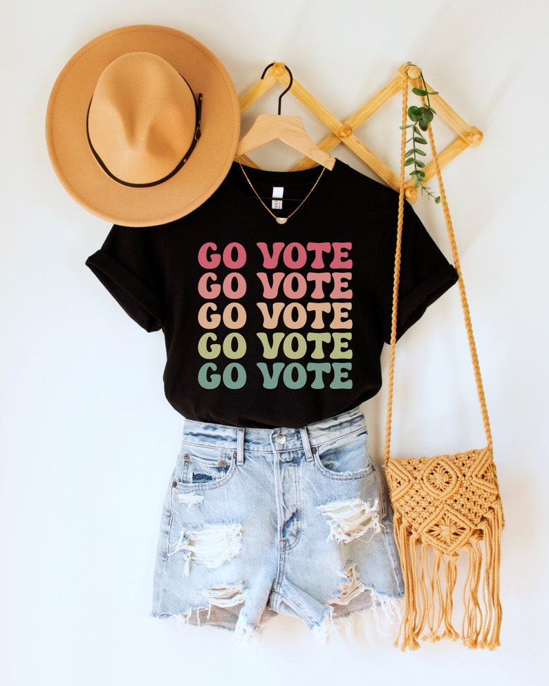 A black unisex crew neck short sleeve t-shirt that says "go vote" repeating 5 times in pastel colors