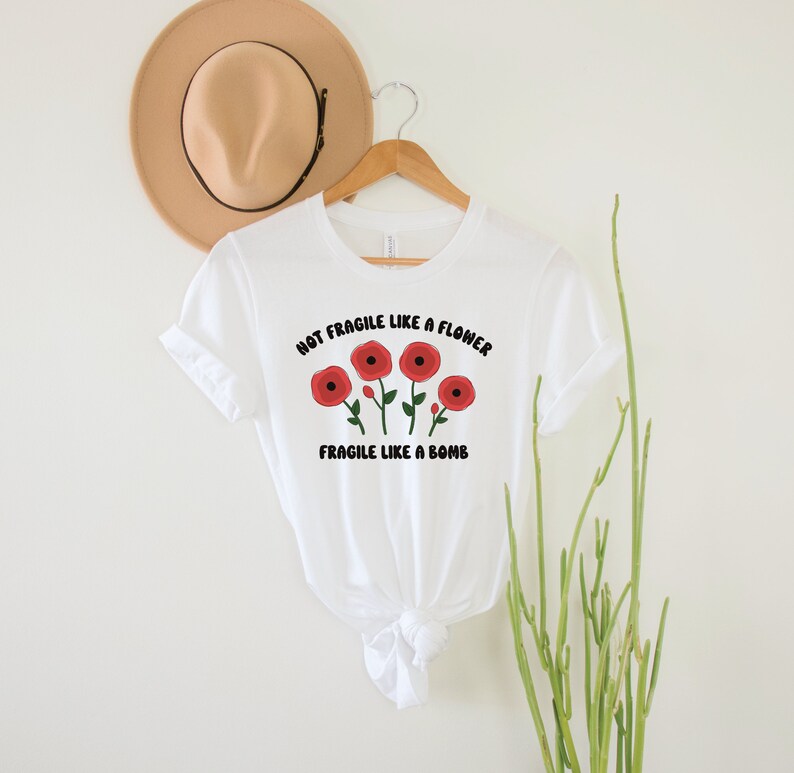 May include: White t-shirt with a graphic of red flowers and the text "Not Fragile Like A Flower Fragile Like A Bomb".