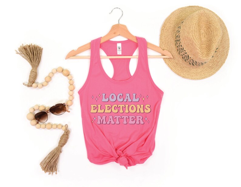A hot pink women’s racerback tank top that says "local elections matter" in purple, yellow, and pink retro text with retro stars