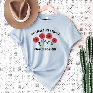 May include: Light blue t-shirt with a graphic of red flowers and the text "Not Fragile Like A Flower Fragile Like A Bomb".