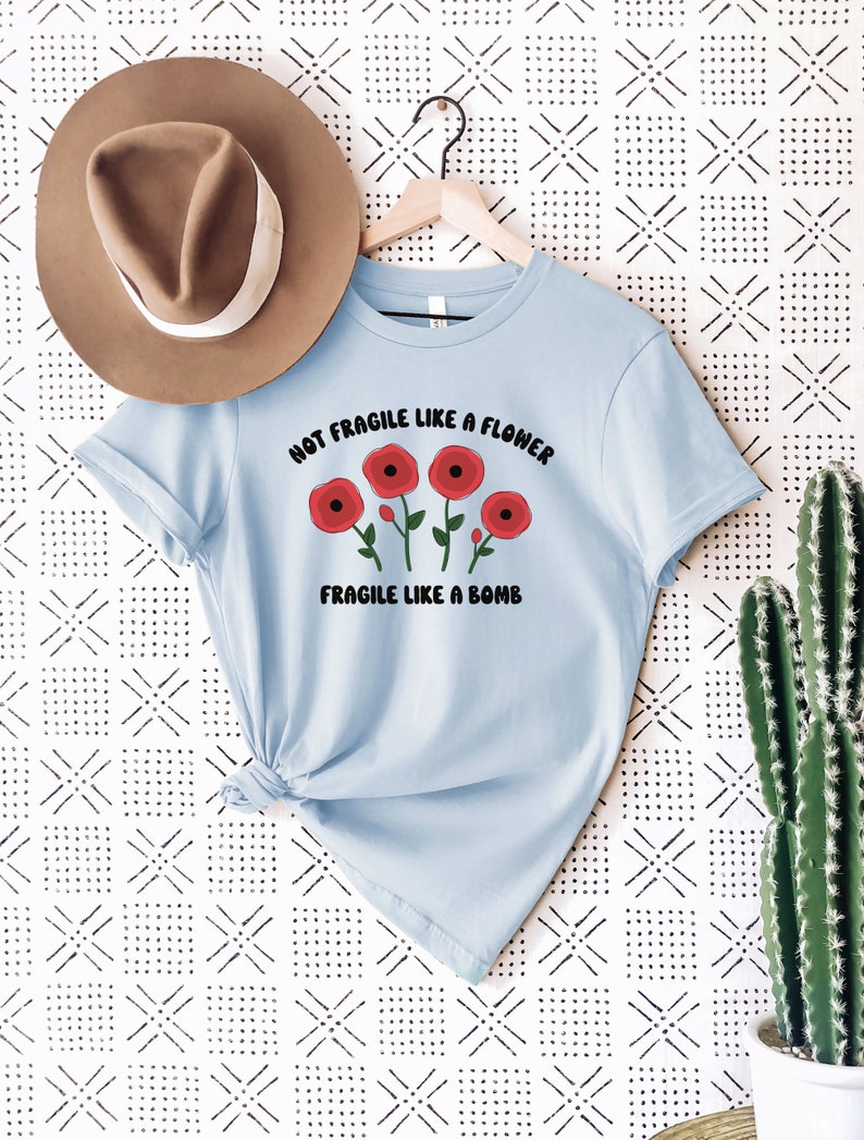 May include: Light blue t-shirt with a graphic of red flowers and the text "Not Fragile Like A Flower Fragile Like A Bomb".