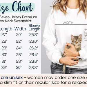May include: A white unisex crew neck sweatshirt with a size chart. The chart lists measurements for sizes S to 3XL, with lengths from 27" to 32", widths from 20" to 30", and sleeve lengths from 25.8" to 26.8". A kitten is held in front of the sweatshirt.