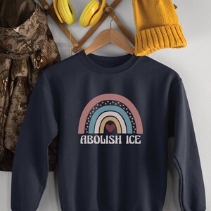 May include: A navy blue sweatshirt with a rainbow graphic and the text "Abolish ICE" in white. A red heart is in the center of the rainbow.