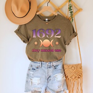 Puede incluir: Una camiseta verde con el texto "1692" y un s&iacute;mbolo de triple luna con estrellas. El texto "they missed one" est&aacute; debajo del s&iacute;mbolo.