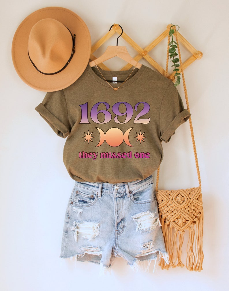 Puede incluir: Una camiseta verde con el texto "1692" y un s&iacute;mbolo de triple luna con estrellas. El texto "they missed one" est&aacute; debajo del s&iacute;mbolo.