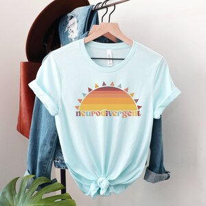 May include: A light blue t-shirt with a retro sunset graphic and the text "neurodivergent" in a colorful font.