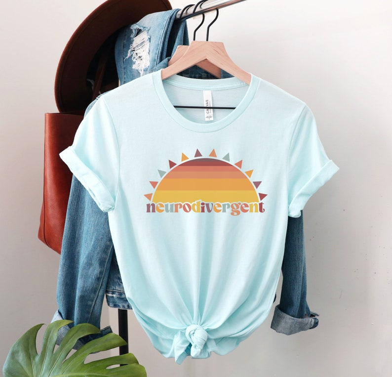 May include: A light blue t-shirt with a retro sunset graphic and the text "neurodivergent" in a colorful font.