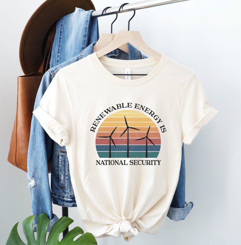 May include: A cream-colored t-shirt with a vintage-style graphic that reads "Renewable Energy is National Security". The graphic features a sunset with three wind turbines.