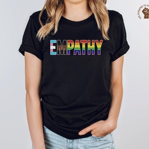 May include: Black t-shirt with the word "EMPATHY" printed in rainbow colors. The letters are outlined in black.