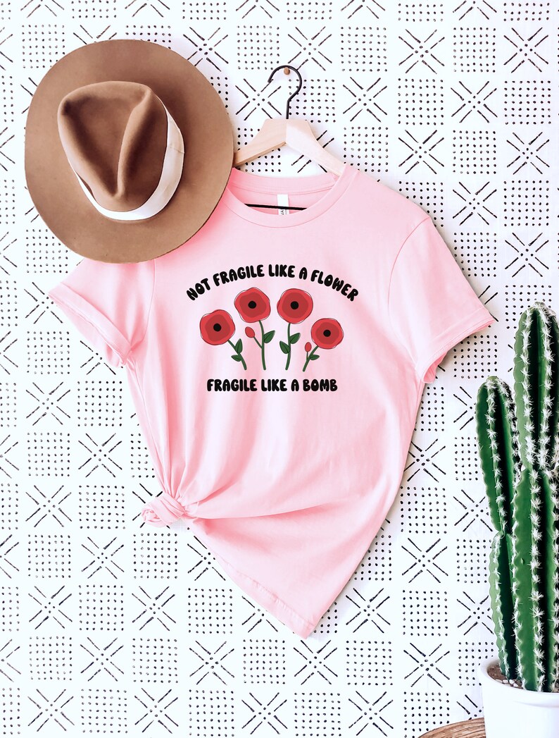 May include: Pink t-shirt with a graphic of red flowers and the text "Not Fragile Like A Flower Fragile Like A Bomb".