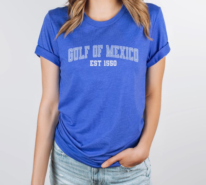 A heather true royal blue unisex crew neck short sleeve Bella+Canvas brand t-shirt that says "GULF OF MEXICO" on the chest in white outline college style font with white stripes inside the letters. The text is curved over smaller solid white letters in the same font that say "EST 1550". The graphic has a distressed/vintage look