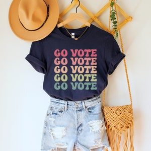 A navy blue unisex crew neck short sleeve t-shirt that says "go vote" repeating 5 times in pastel colors