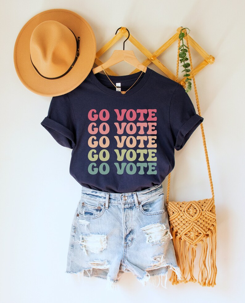 A navy blue unisex crew neck short sleeve t-shirt that says "go vote" repeating 5 times in pastel colors