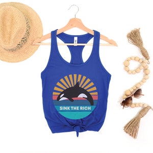 A royal blue women's racerback tank top that says "sink the rich" in white over a retro graphic of an orca whale in the ocean