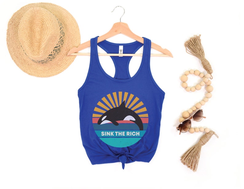 A royal blue women's racerback tank top that says "sink the rich" in white over a retro graphic of an orca whale in the ocean