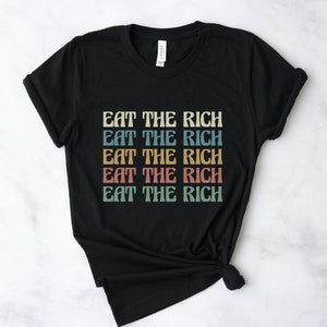 A black unisex crew neck short sleeve Bella Canvas t-shirt that says "eat the rich" repeated 5 times in retro font and colors