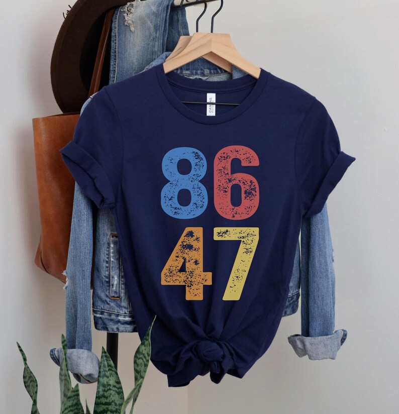 A navy blue unisex crew neck short sleeve Bella+Canvas t-shirt that says "86 47" on the front in large bold distressed numbers, with a blue 8, red 6, orange 4, and yellow 7