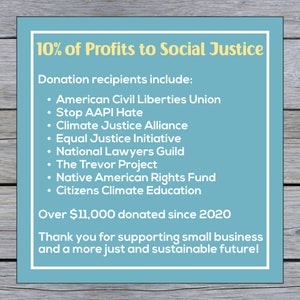 May include: A blue and white sign with the text "10% of Profits to Social Justice". The sign lists organizations that receive donations, including the American Civil Liberties Union, Stop AAPI Hate, Climate Justice Alliance, Equal Justice Initiative, National Lawyers Guild, The Trevor Project, Native American Rights Fund, and Citizens Climate Education. The sign also states that over $11,000 has been donated since 2020.