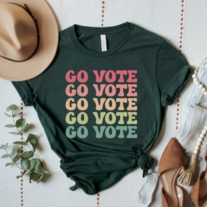 A forest (dark green) unisex crew neck short sleeve t-shirt that says "go vote" repeating 5 times in pastel colors