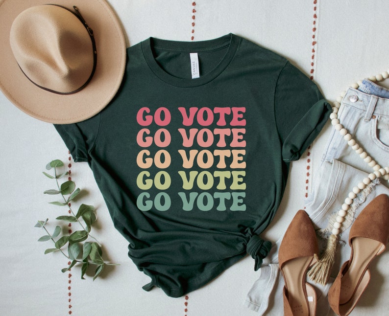 A forest (dark green) unisex crew neck short sleeve t-shirt that says "go vote" repeating 5 times in pastel colors