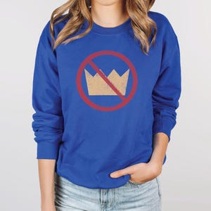 A royal blue unisex crew neck long sleeve fleece-lined sweatshirt with an image of a yellow crown inside a red circle with a slash over it, meaning "no kings". The image has a vintage/distressed look.