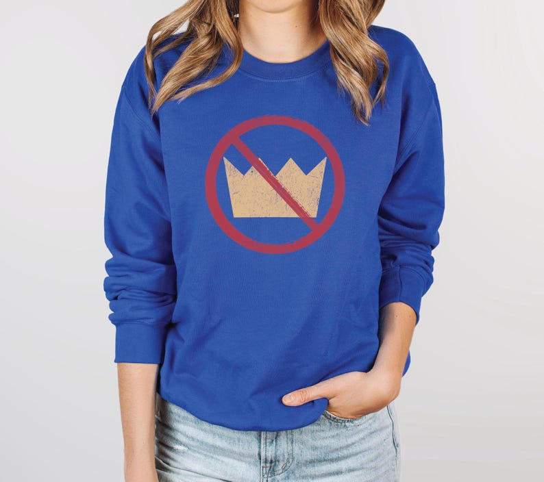 A royal blue unisex crew neck long sleeve fleece-lined sweatshirt with an image of a yellow crown inside a red circle with a slash over it, meaning "no kings". The image has a vintage/distressed look.