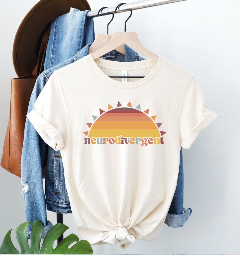May include: A cream colored t-shirt with a retro sunset graphic and the text "neurodivergent" in colorful letters.