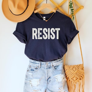 A navy blue unisex crew neck short sleeve Bella+Canvas t-shirt that says "RESIST" in distressed white tall block text