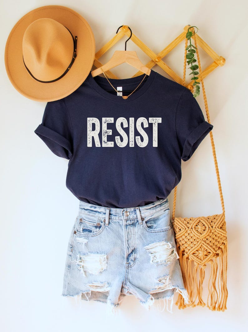 A navy blue unisex crew neck short sleeve Bella+Canvas t-shirt that says "RESIST" in distressed white tall block text
