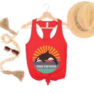 A red women's racerback tank top that says "sink the rich" in white over a retro graphic of an orca whale in the ocean