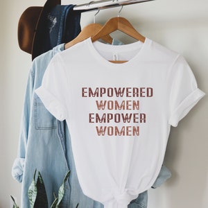 May include: White t-shirt with the text "EMPOWERED WOMEN EMPOWER WOMEN" printed in brown and pink.