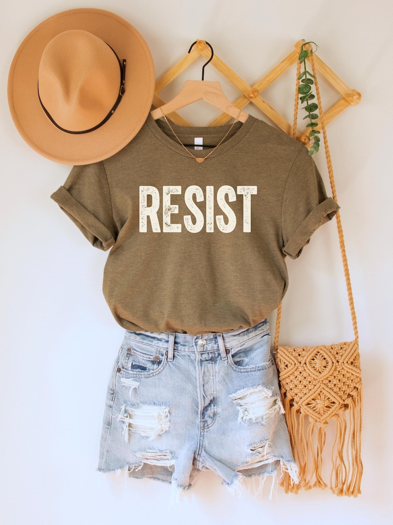 A heather olive green/brown unisex crew neck short sleeve Bella+Canvas t-shirt that says "RESIST" in distressed white tall block text