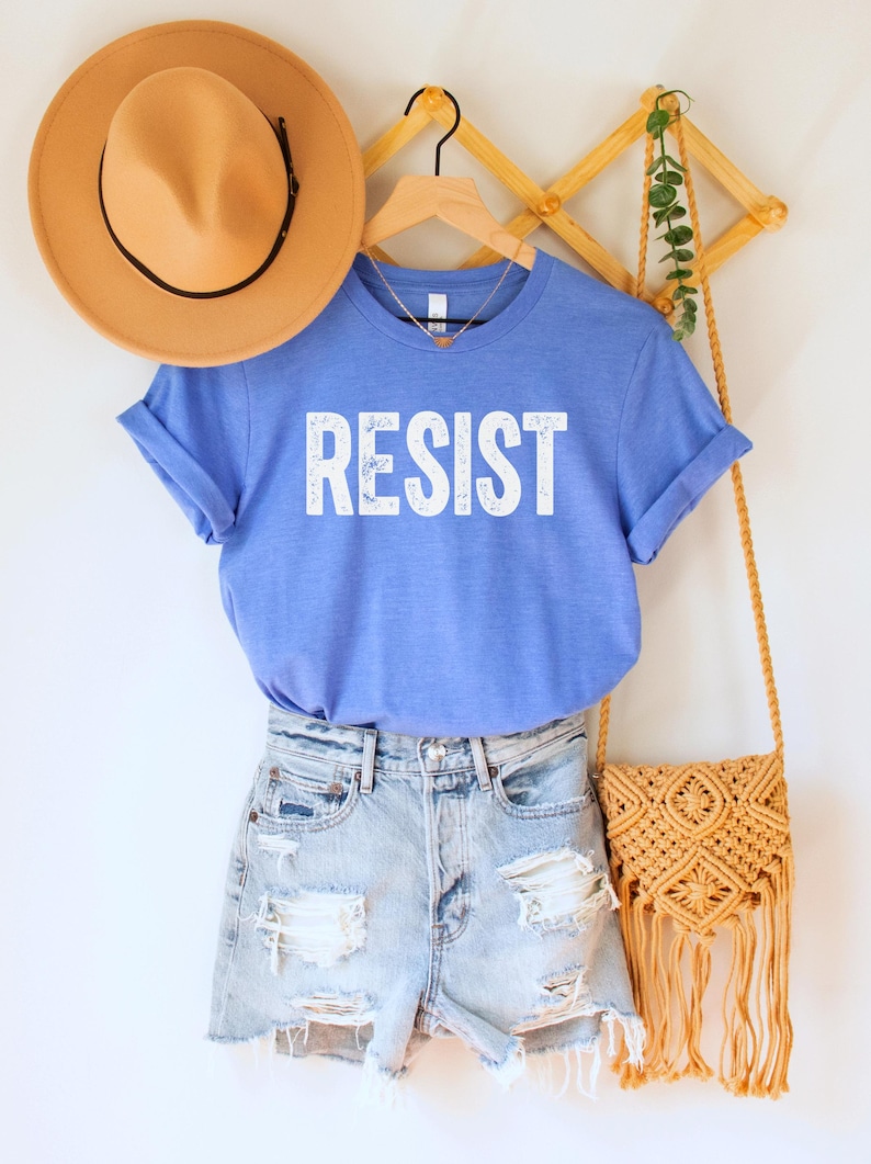 A heather Columbia (medium) blue unisex crew neck short sleeve Bella+Canvas t-shirt that says "RESIST" in distressed white tall block text