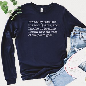 A navy blue unisex long sleeve crew neck t-shirt that says "First they came for the immigrants, and I spoke up because I know how the rest of the poem goes." in white typewriter font on the chest.