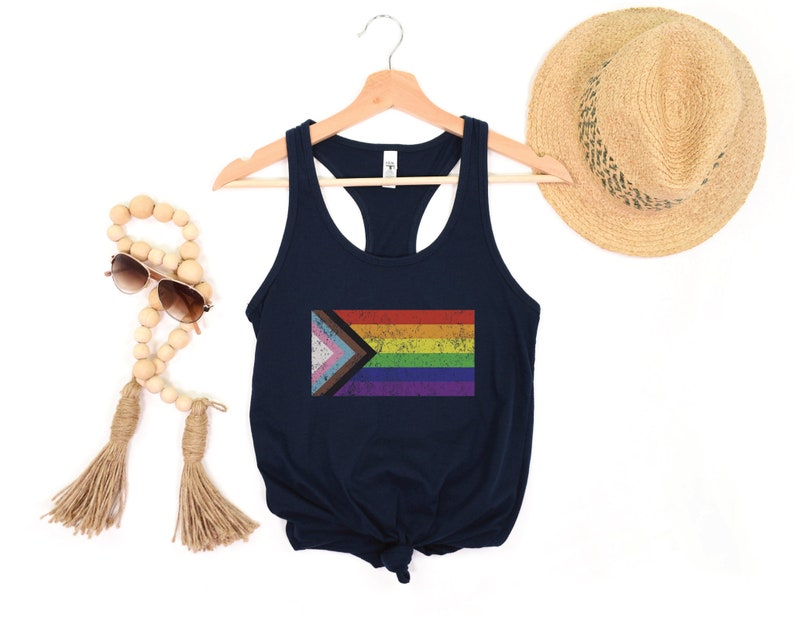 May include: A navy blue racerback tank top with a distressed, rainbow pride flag design. The flag includes the colors of the traditional rainbow flag, as well as the colors of the transgender pride flag.