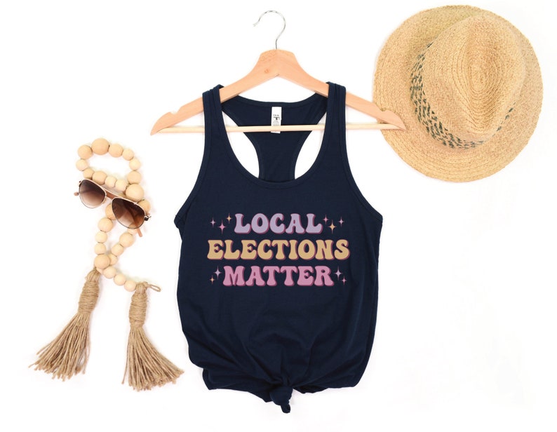 A navy blue women’s racerback tank top that says "local elections matter" in purple, yellow, and pink retro text with retro stars
