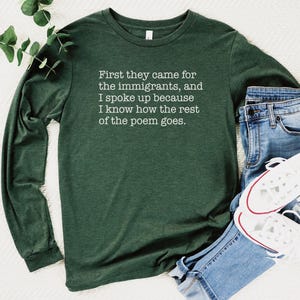 A heather forest green unisex long sleeve crew neck t-shirt that says "First they came for the immigrants, and I spoke up because I know how the rest of the poem goes." in white typewriter font on the chest.