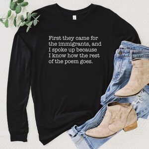 A black unisex long sleeve crew neck t-shirt that says "First they came for the immigrants, and I spoke up because I know how the rest of the poem goes." in white typewriter font on the chest.