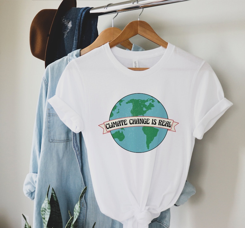 May include: White t-shirt featuring a graphic of a blue and green Earth with the text "Climate Change is Real" on a red banner.
