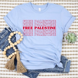 A baby blue unisex crew neck t-shirt with red text saying "Free Palestine" 5 times, with the middle text full red and the top and bottom 2 just a red outline
