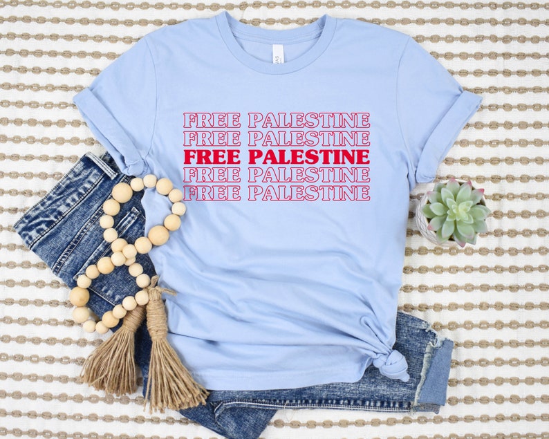 A baby blue unisex crew neck t-shirt with red text saying "Free Palestine" 5 times, with the middle text full red and the top and bottom 2 just a red outline