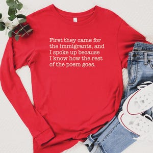 A red unisex long sleeve crew neck t-shirt that says "First they came for the immigrants, and I spoke up because I know how the rest of the poem goes." in white typewriter font on the chest.