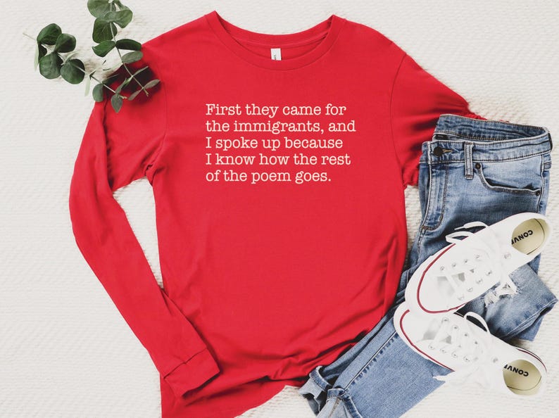 A red unisex long sleeve crew neck t-shirt that says "First they came for the immigrants, and I spoke up because I know how the rest of the poem goes." in white typewriter font on the chest.
