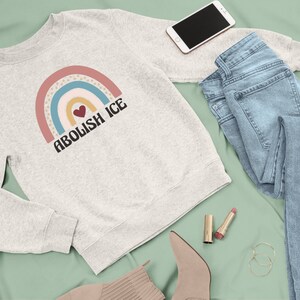 May include: A grey sweatshirt with a rainbow graphic and the text "Abolish ICE" in black. A heart is in the center of the rainbow.