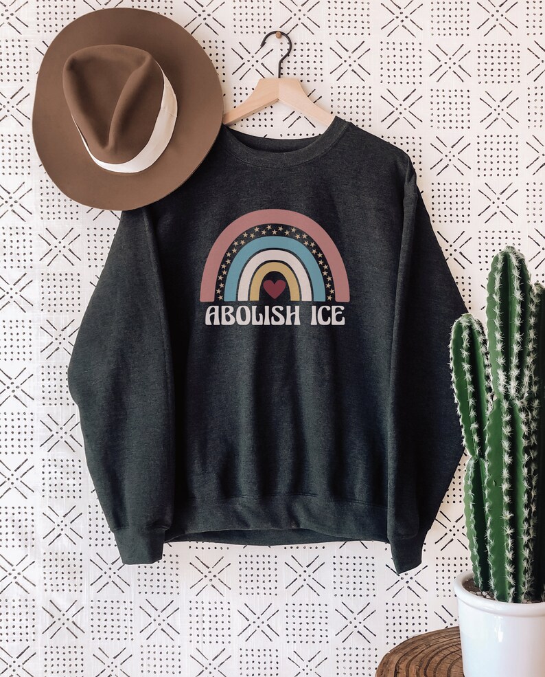 May include: A dark grey sweatshirt with a rainbow graphic and the text "ABOLISH ICE" in white. The rainbow has a red heart in the center.