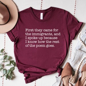 A maroon unisex short sleeve crew neck t-shirt that says "First they came for the immigrants, and I spoke up because I know how the rest of the poem goes." in white typewriter font on the chest.