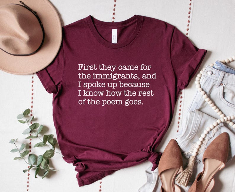 A maroon unisex short sleeve crew neck t-shirt that says "First they came for the immigrants, and I spoke up because I know how the rest of the poem goes." in white typewriter font on the chest.