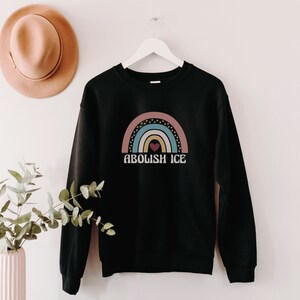 May include: Black sweatshirt with a rainbow graphic and the text "Abolish ICE" in white.