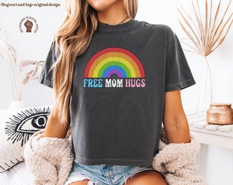 May include: Dark gray t-shirt with a rainbow graphic and the text "Free Mom Hugs" in colorful letters. The shirt is a casual style, suitable for everyday wear. The design features a rainbow arching over the text.
