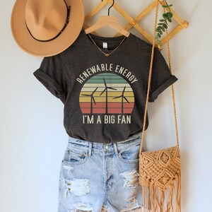 May include: A dark grey t-shirt with a vintage-style graphic of wind turbines in front of a sunset. The text "Renewable Energy I'm a Big Fan" is printed on the shirt.